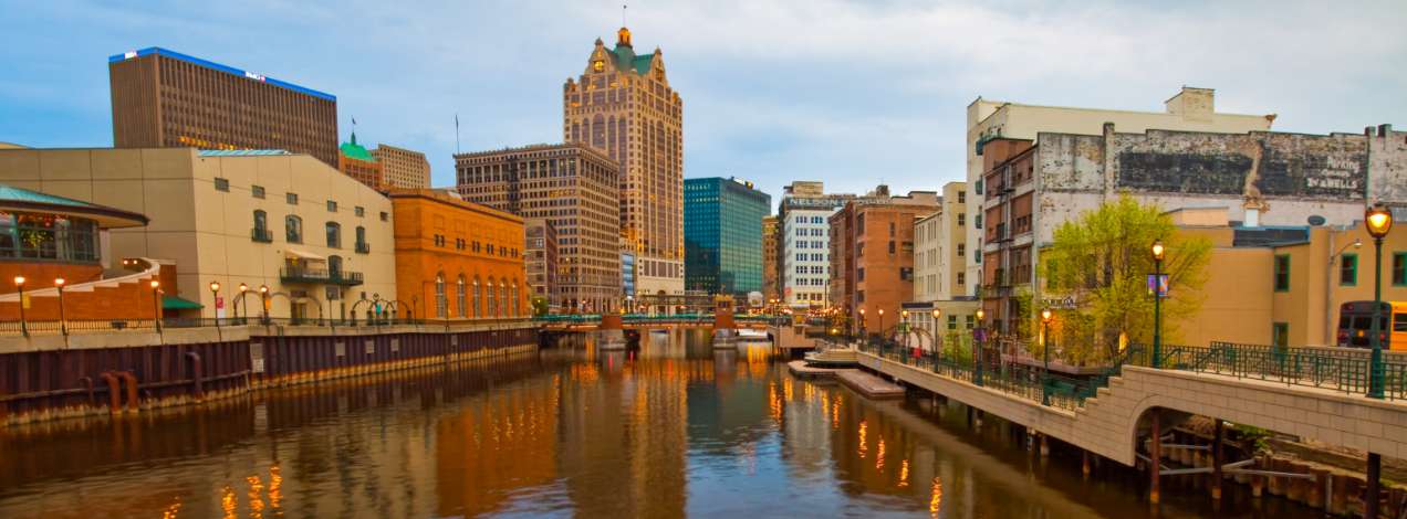 The Milwaukee River winding through downtown Milwaukee, Wisconsin, framed by the city's distinct architectural mix including the historic Milwaukee City Hall tower in the background.