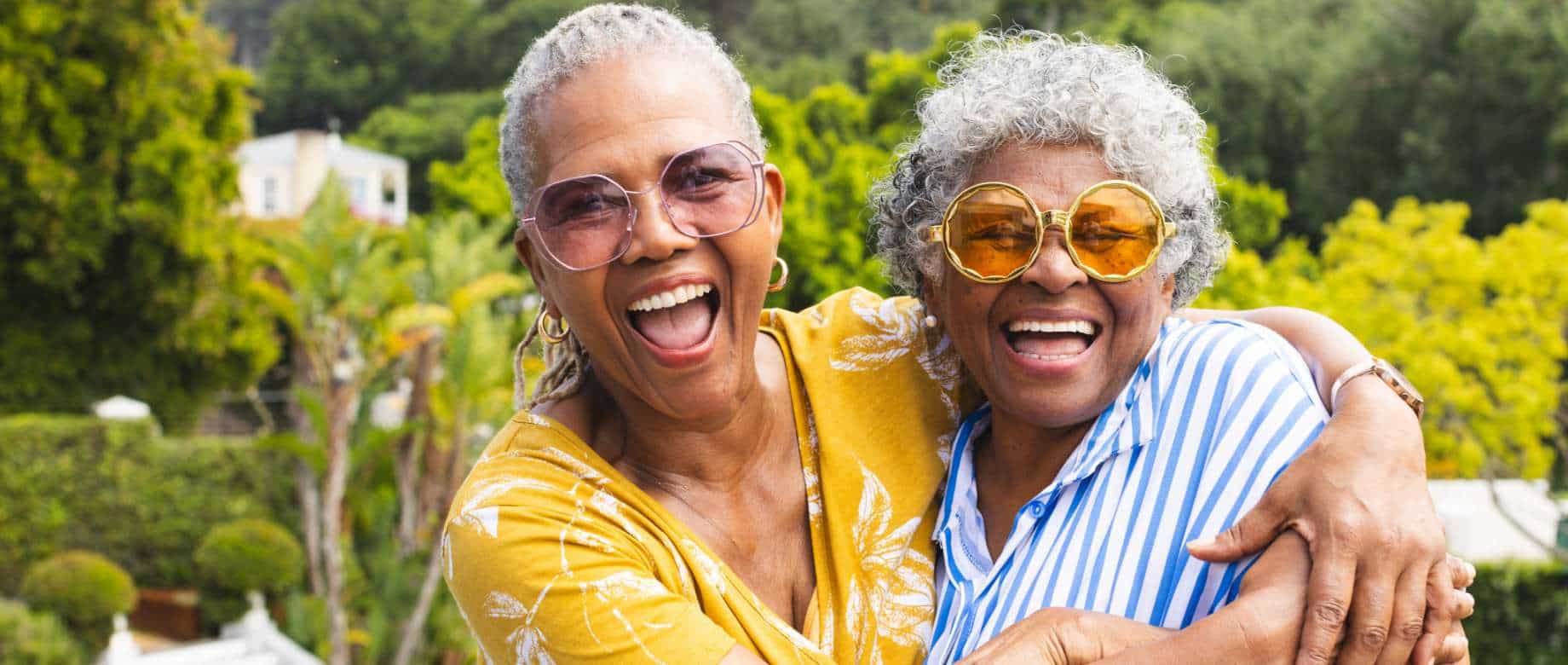 Two older women hugging in a garden and laughing