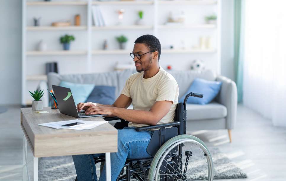 A smiling man in a wheelchair receiving SSDI application assistance from Advocator Advantage on his laptop.